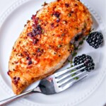 A blackberry chicken breast on a white plate with a fork and two blackberries