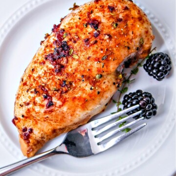 A blackberry chicken breast on a white plate with a fork and two blackberries