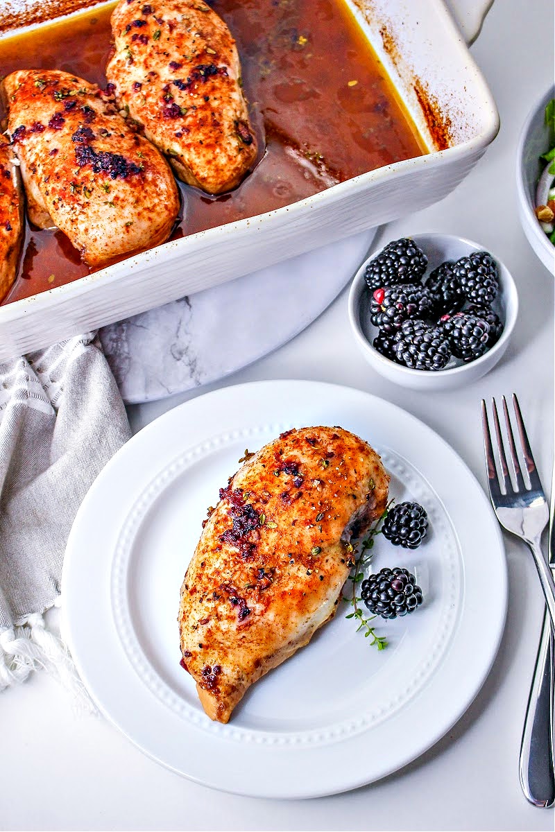 A casserole dish with blackberry chicken and a white plate holding one serving of blackberry chicken