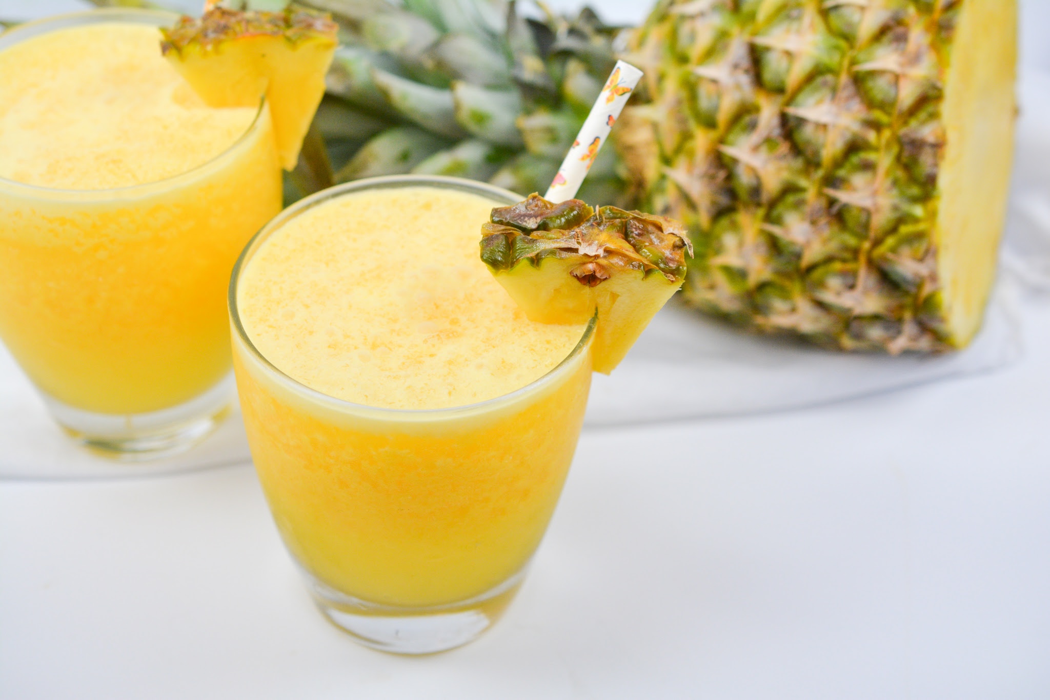 Two Keto Pina Coladas in front of half of a fresh pineapple
