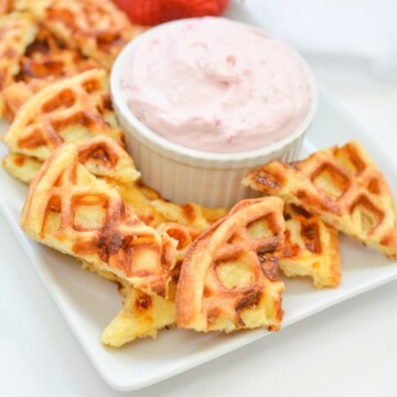 A plate of chaffle chips with three strawberries on it with a bowl of strawberry dip