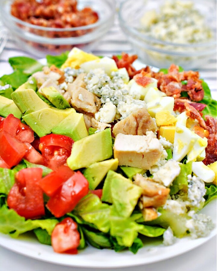 Keto Cheesecake Factory Chopped Salad on a white plate in front of a bowl of bacon