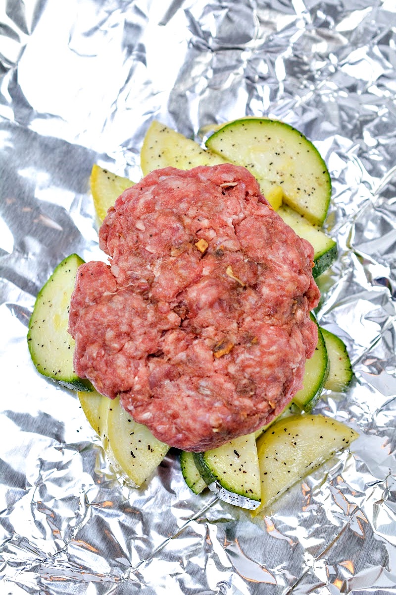 Raw burger on top of veggies in a foil packet
