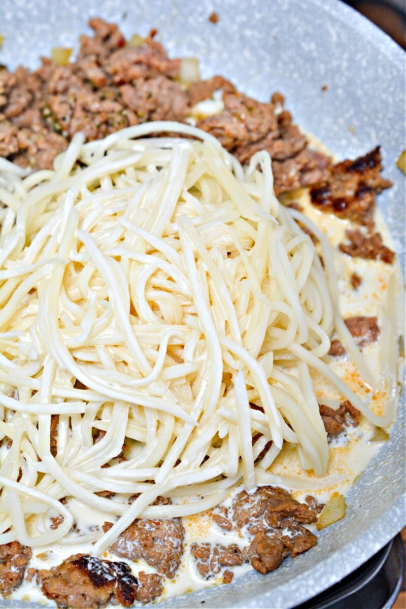 Adding noodles to the skillet with the sausage