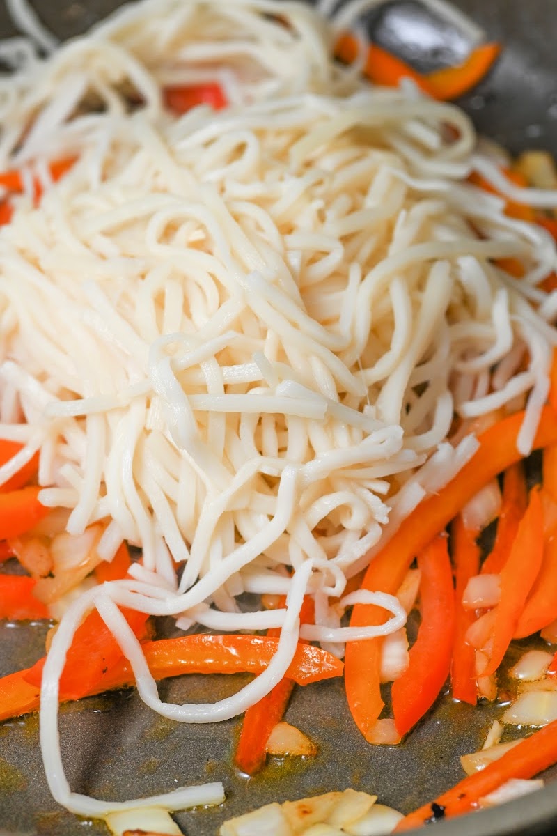 Adding noodles to the peppers and onions